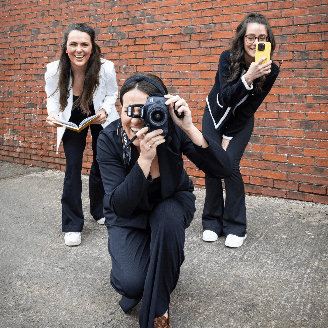 Three Creative Collings team members one holding a book, one holding and point a camera and one holding and pointing a mobile