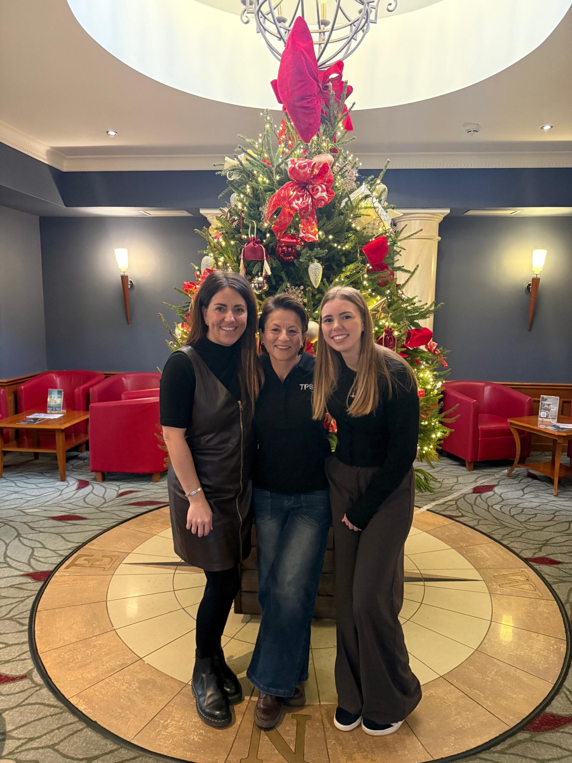 Natalie standing in front of a Christmas tree with two members of the tps360