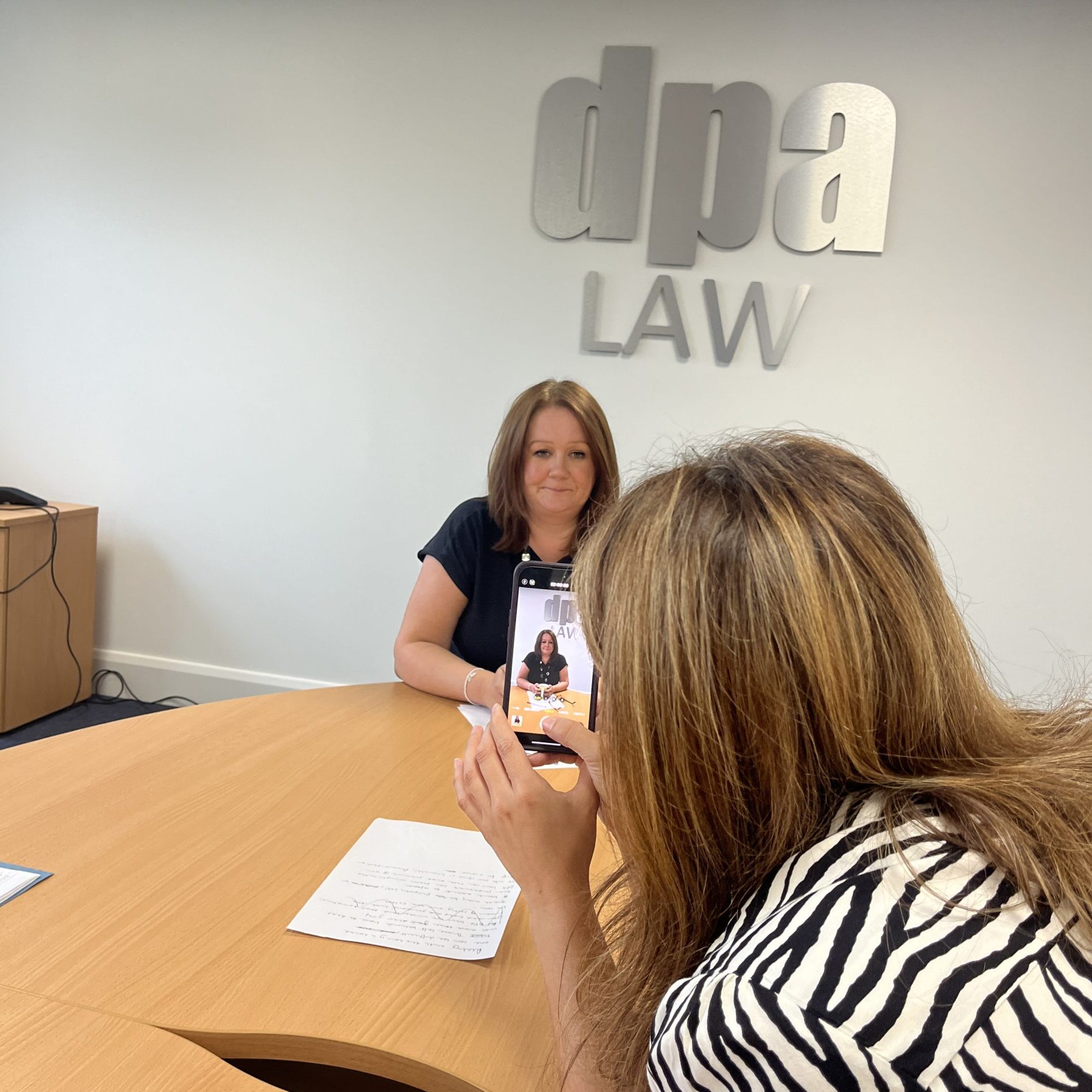 Two ladies sitting in a office showing a mobile screen advertising dpa Law