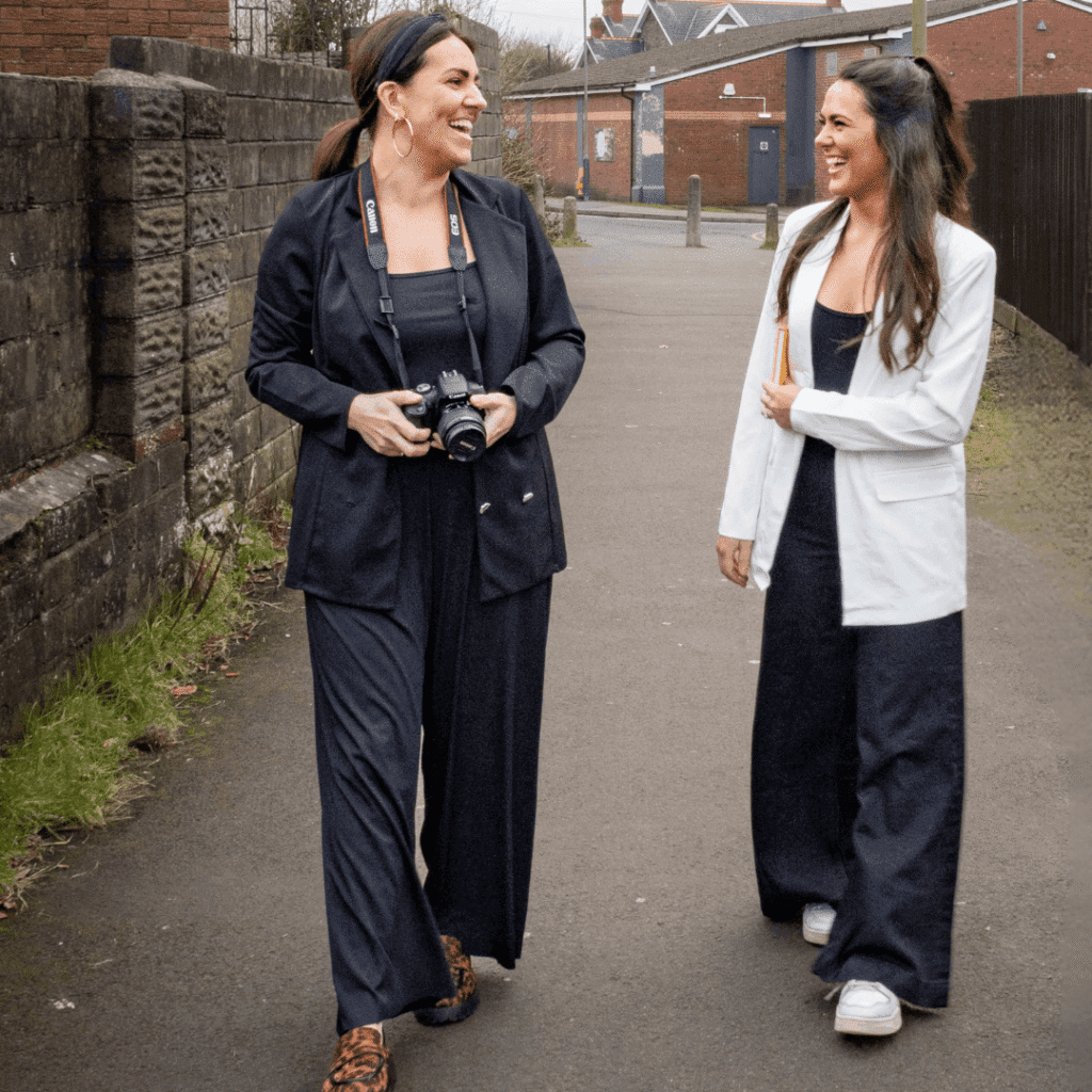 Natalie and a team member walking forward along a street. Natalie is holding a camera