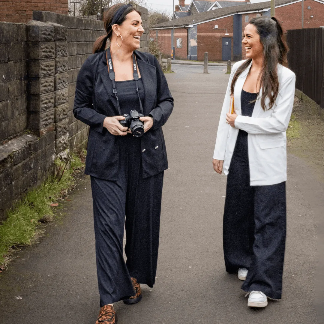 Natalie and a team member walking forward along a street. Natalie is holding a camera